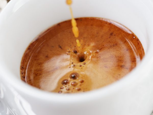 extraction of espresso with rich crema in cup, close up photo