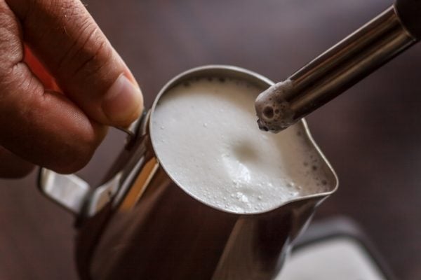 Professional bartender warming milk for cappuccino. Barista using coffee machine for latte art macchiato. Toned image.